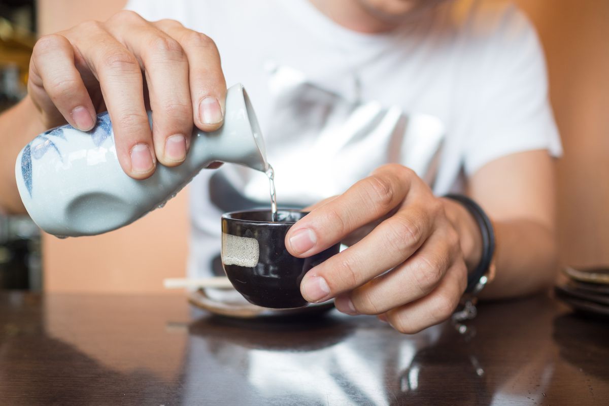 A closeup of a man pouring sake into a ceramic cup.