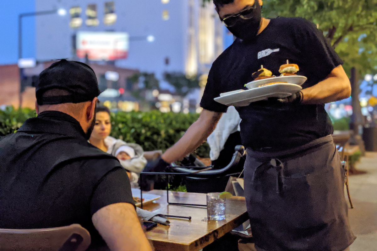 Server places dishes at an outdoor dining table in Glendale, CA.