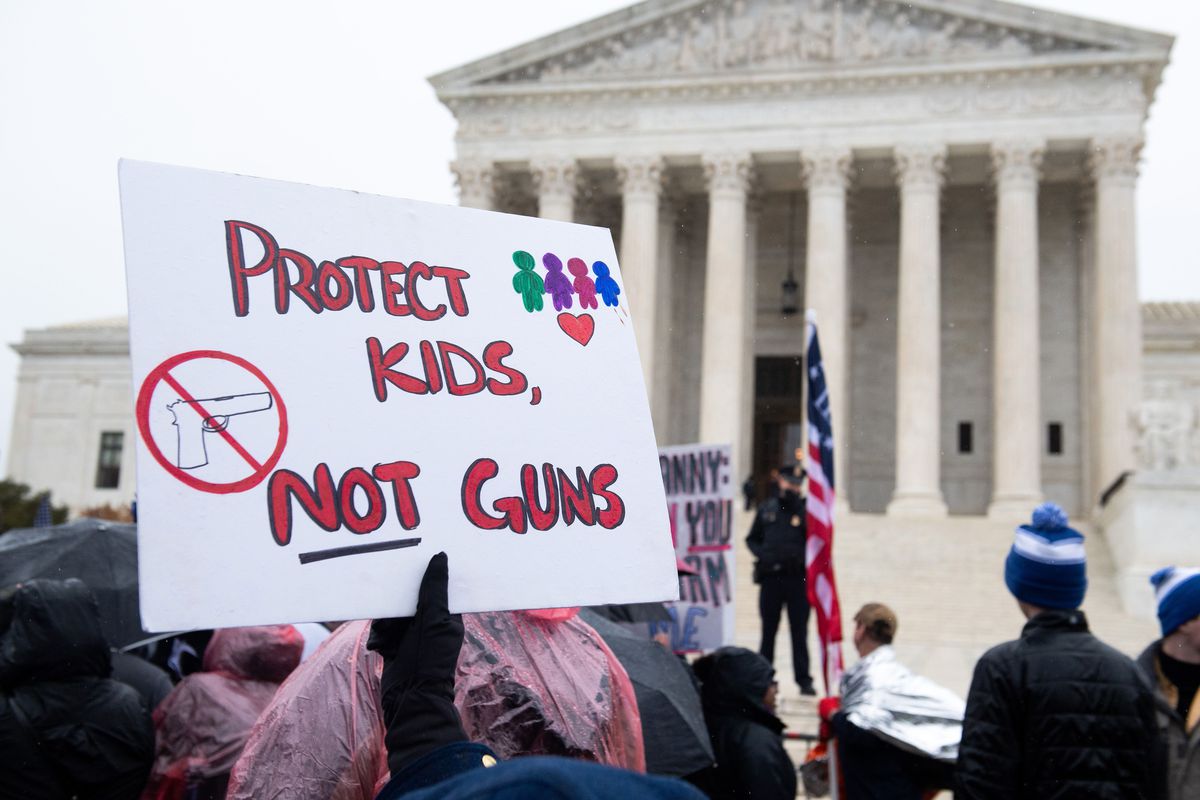 A protester outside the Supreme Court building holds a sign that reads, “Protect kids, not guns.”