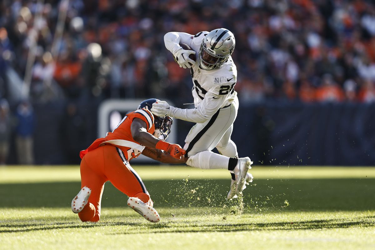 Josh Jacobs #28 of the Las Vegas Raiders runs and leaps against Damarri Mathis #27 of the Denver Broncos during an NFL game between the Las Vegas Raiders and Denver Broncos at Empower Field At Mile High on November 20, 2022 in Denver, Colorado.