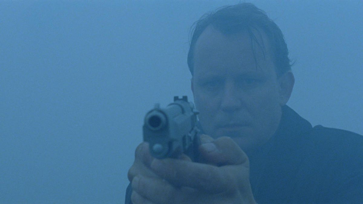Un plano medio de un hombre sosteniendo una pistola rodeado de niebla.