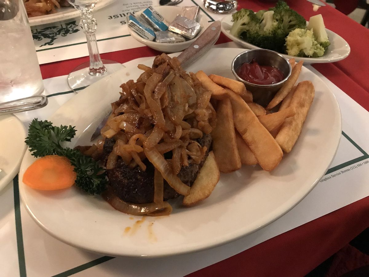 A plate with chopped steak topped with onions and served with a side of fries.