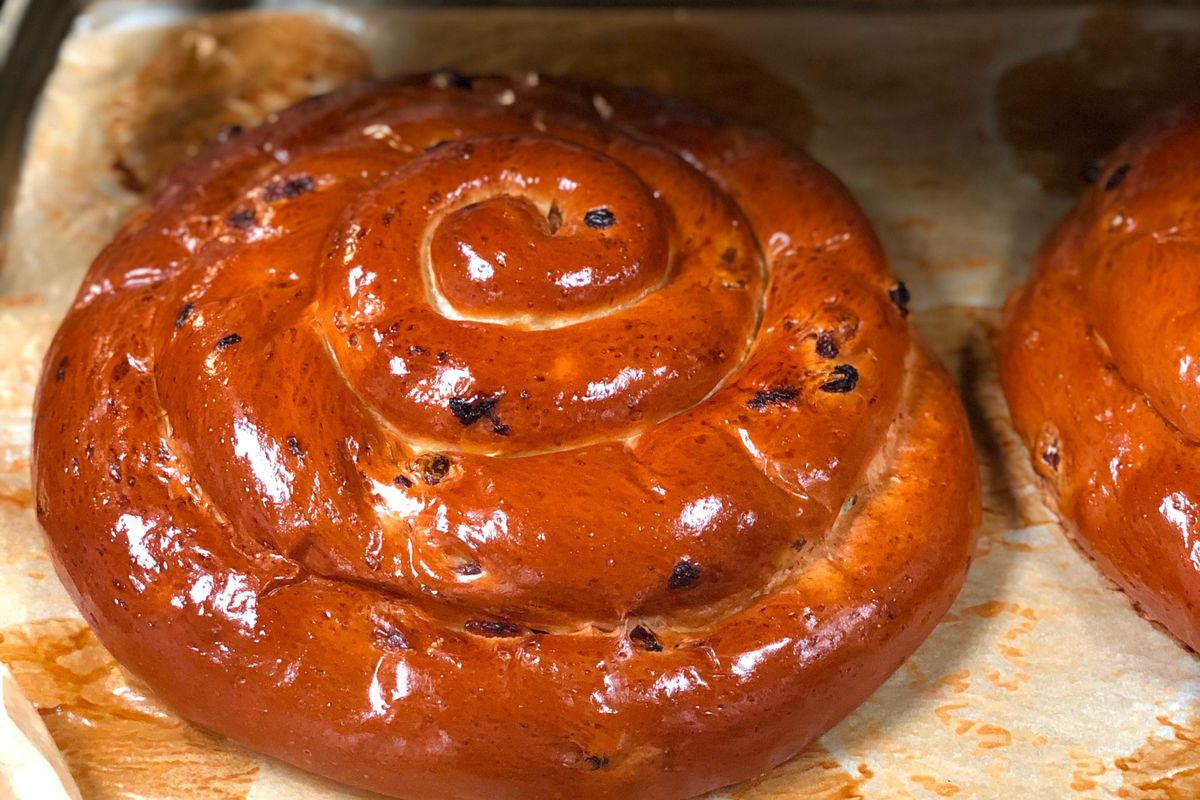 Round challah with raisins sits on a piece of butcher paper and glistens.