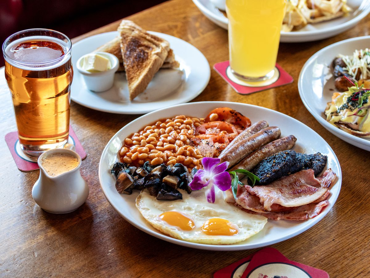 An English breakfast with baked beans, blood sausage, sunny side-up eggs, and ham, with pints of beer at Red Lion Pub.