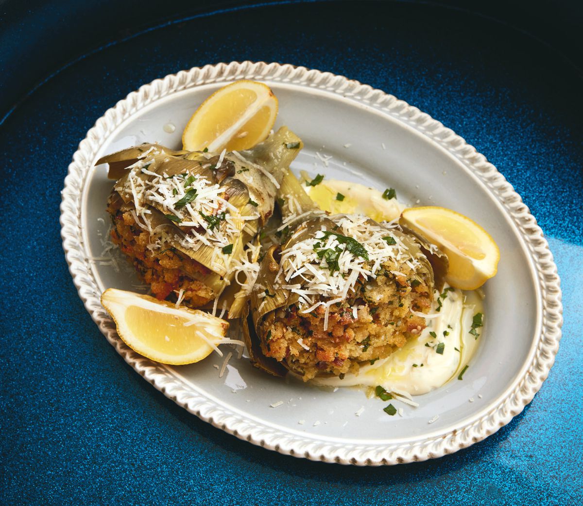 white plate with two stuffed artichokes and slices of lemon