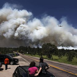 People pulled to over watch from their cars as a fire-fighting slurry plane makes a pass in preparation to drop its load on a wildfire in the Black Forest area north of Colorado Springs, Colo., on Wednesday, June 12, 2013. The number of houses destroyed by the Black Forest fire could grow to around 100, and authorities fear it's possible that some people who stayed behind might have died. (AP Photo/Brennan Linsley)