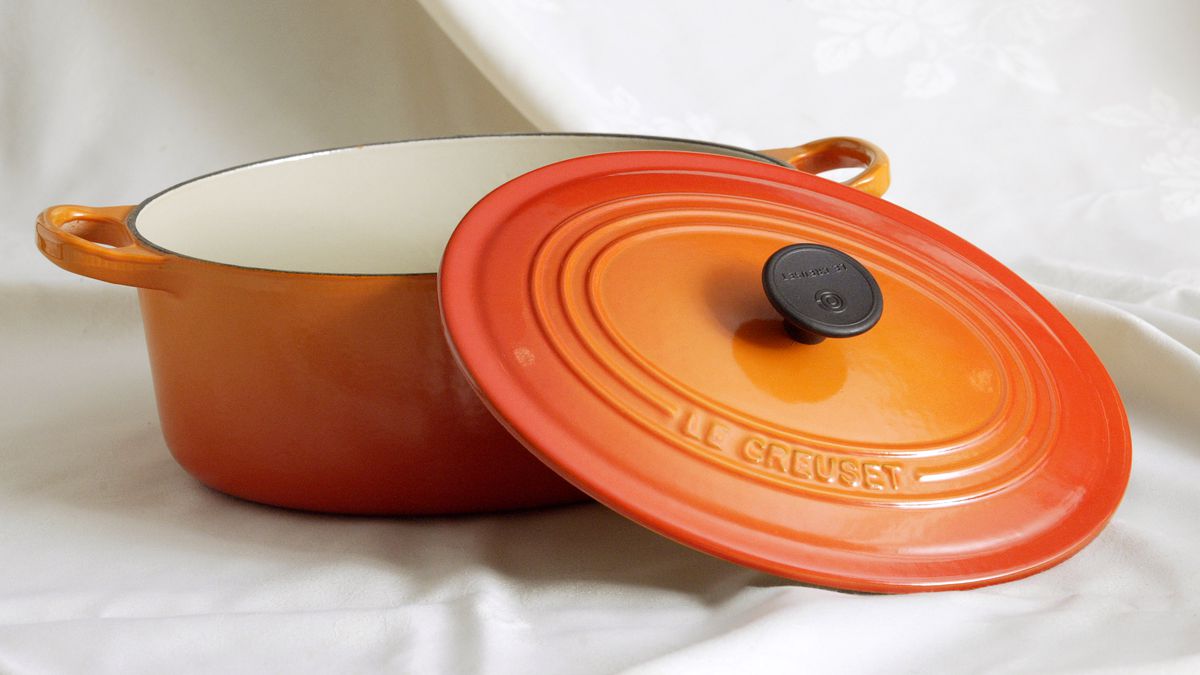 Orange Le Creuset Dutch oven, sitting on ivory tablecloth with top half off 