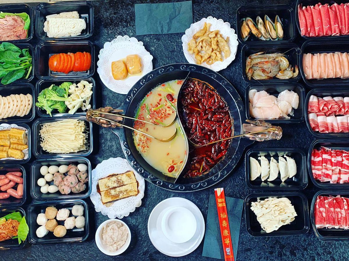 A hot pot full of broth, surrounded by meats and vegetables. 