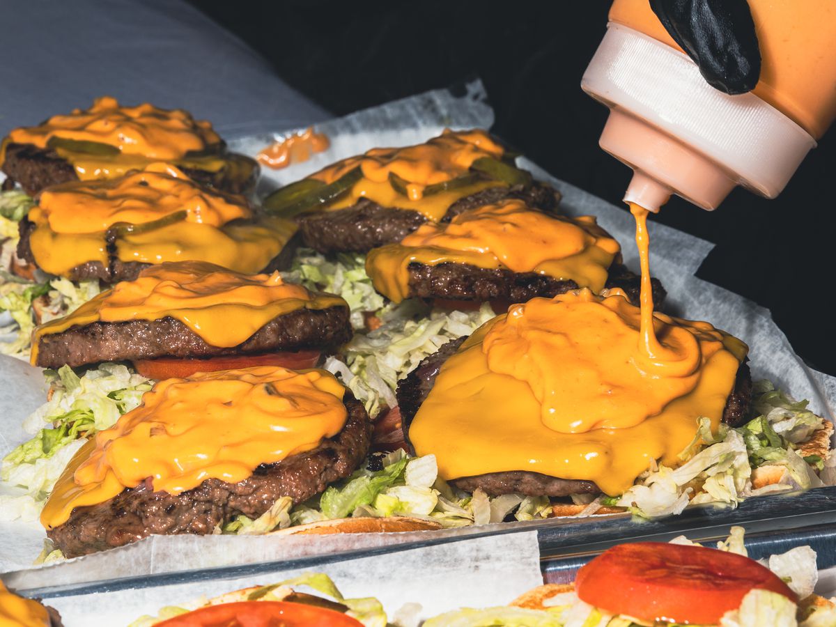 An orange sauce is drizzled onto several burgers at once.