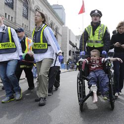 A Boston police officer wheels in injured boy down Boylston Street as medical workers carry an injured runner following an explosion during the 2013 Boston Marathon in Boston, Monday, April 15, 2013. Two explosions shattered the euphoria at the marathon's finish line on Monday, sending authorities out on the course to carry off the injured while the stragglers were rerouted away from the smoking site of the blasts. 