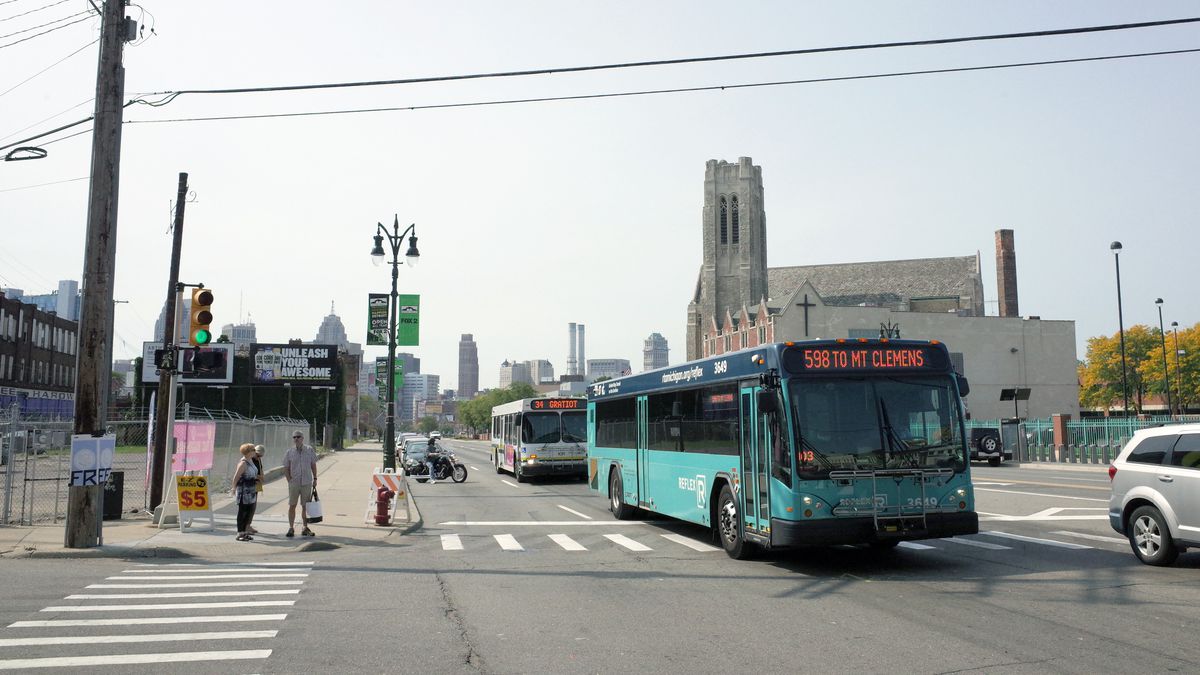 A street in Detroit. There is a blue bus and cars traveling on the street.