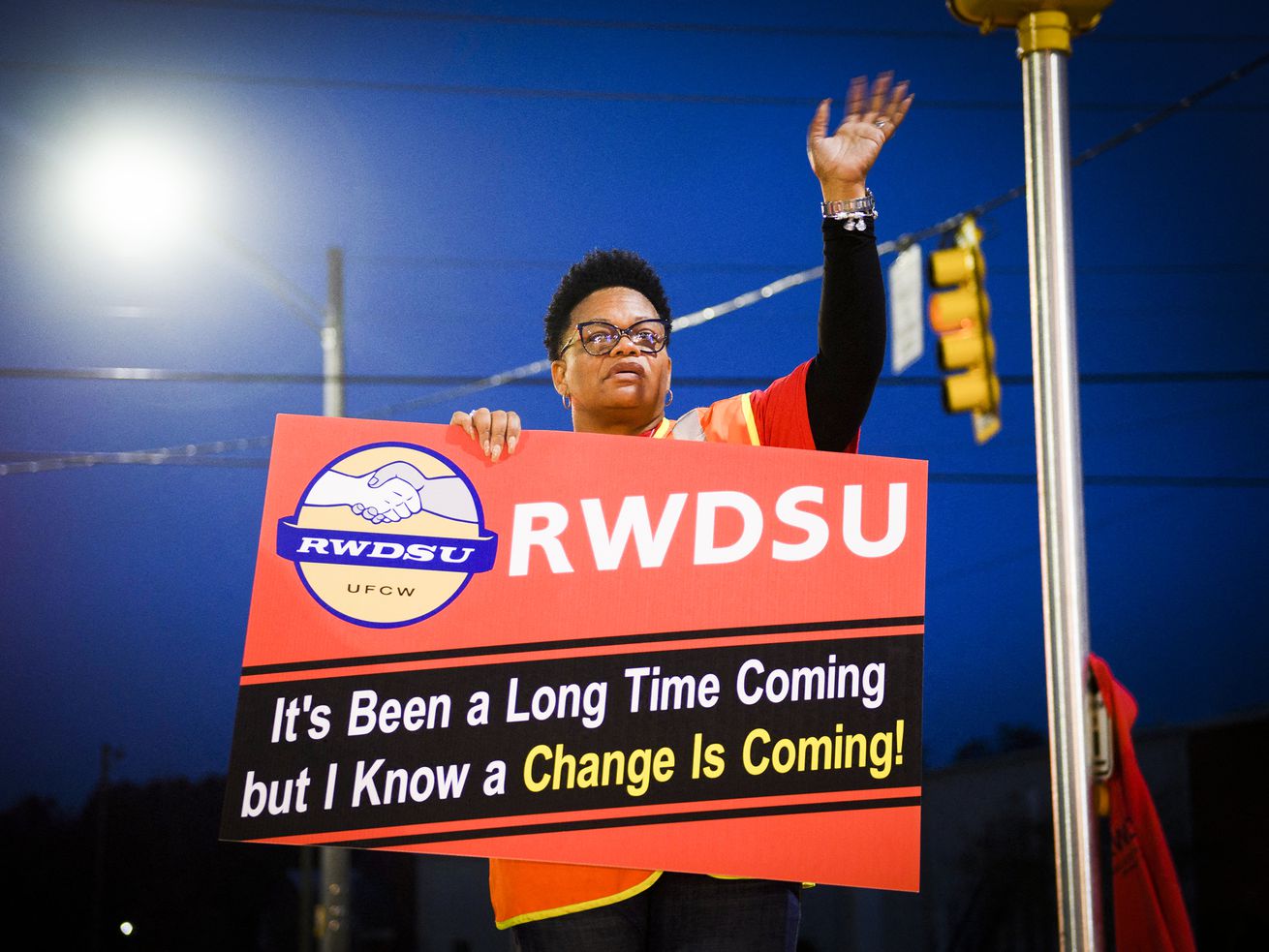 A union organizer holds a sign that reads, “RWDSU. It’s been a long time coming but I know a change is coming!”