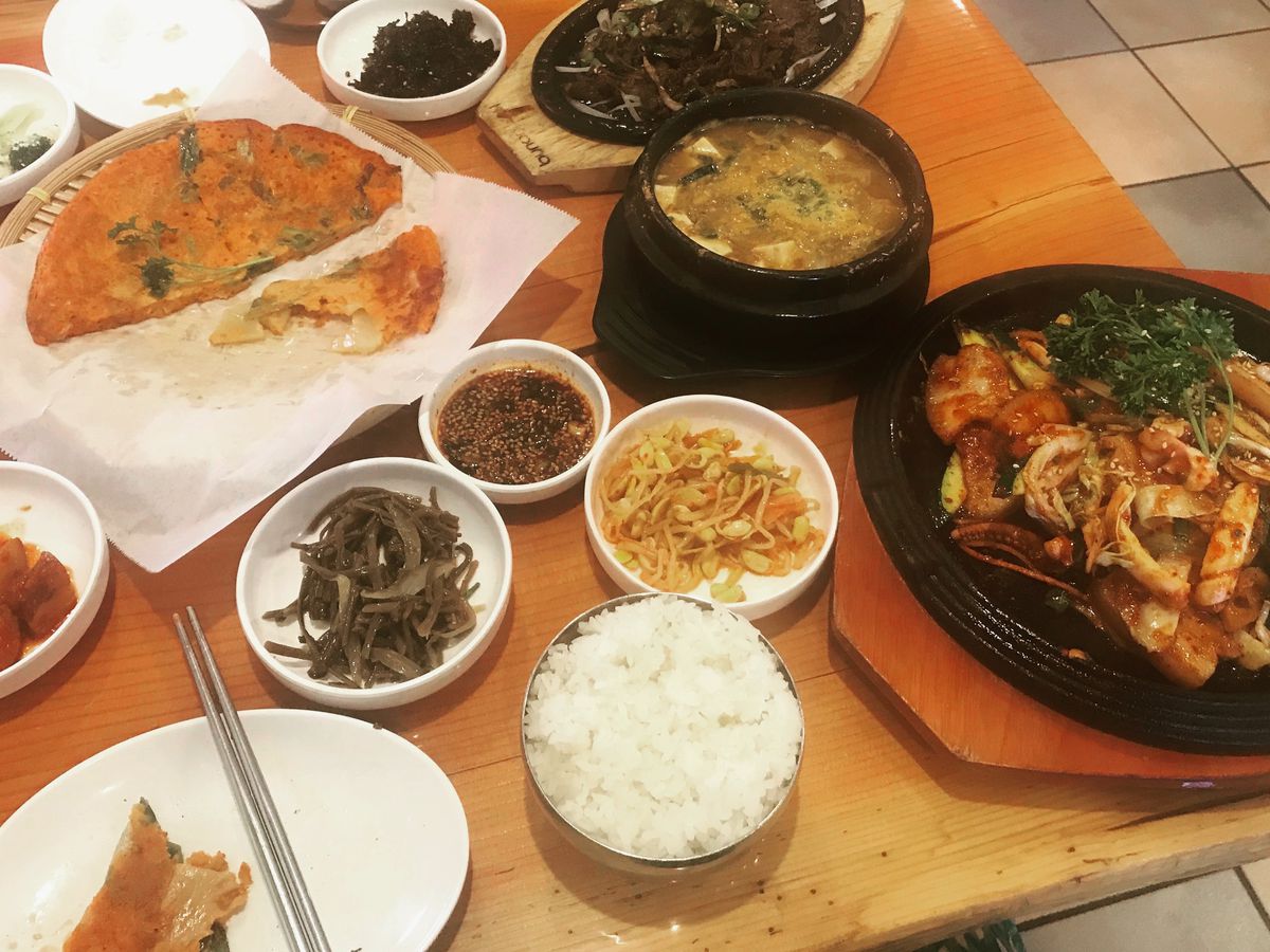 A table with seafood pancakes, banchan, and a pot of doenjang jjigae.
