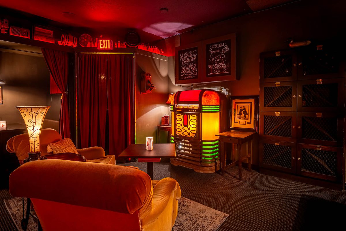 A jukebox glows in the dark Rendition Room with velvet curtains.