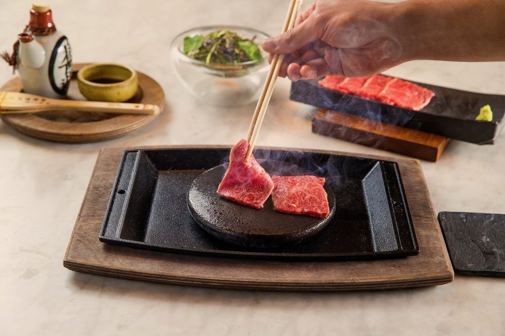 Austere pieces of Kobe beef cooking on a hot plate, tableside.  