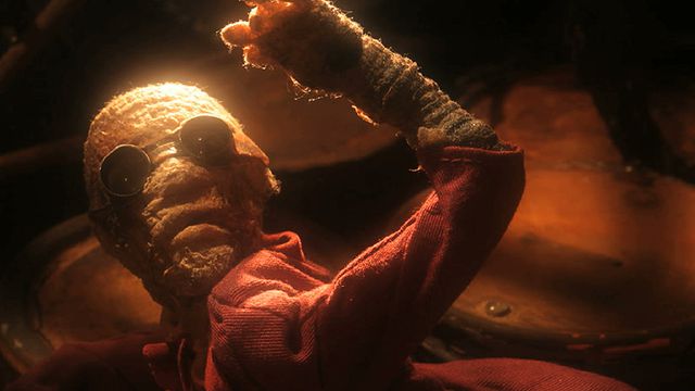 A mummy-like puppet creature in a red coat and sunglasses, about to be hacked up in Phil Tippett’s stop-motion movie Mad God