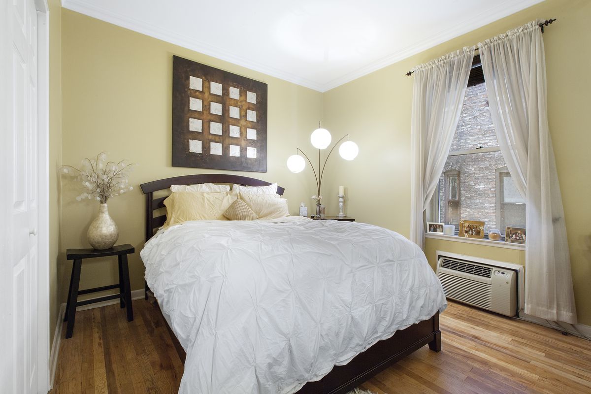 A bedroom with yellow walls, hardwood floors, a large window, and a large bed.