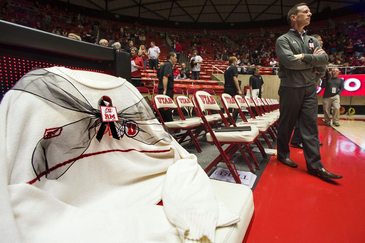 Utah Utes assistant coach Tommy Connor watches warm-ups near a patch and sweater remembering the recently deceased former Utes head coach Rick Majerus on an empty chair.
