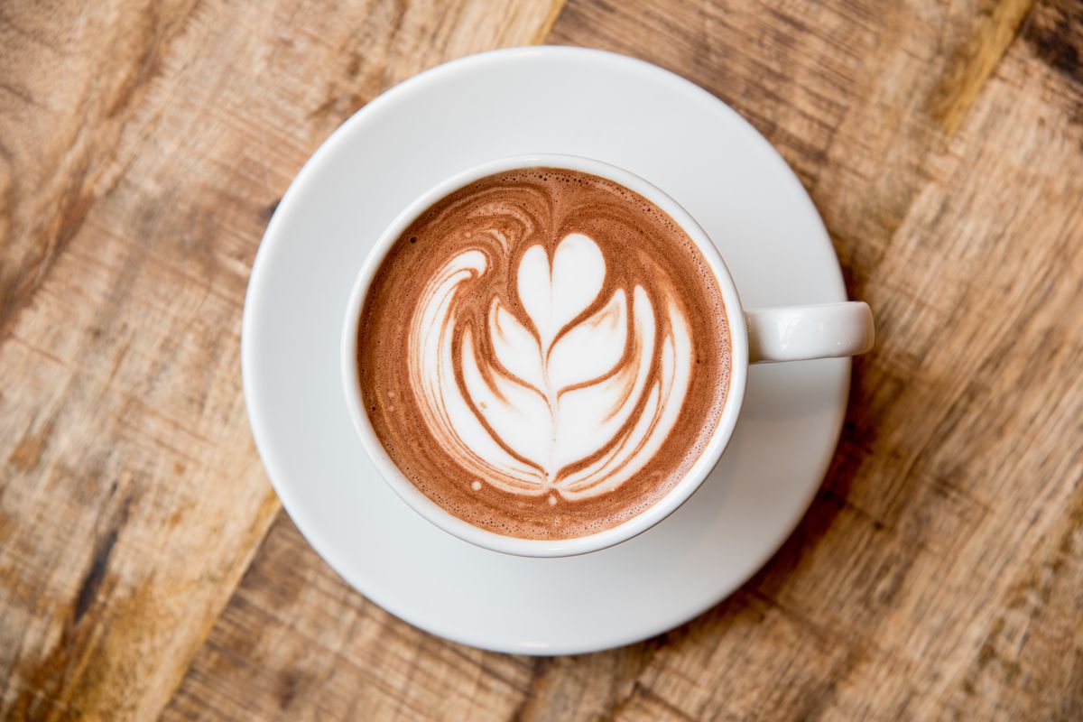 A large white mug holds dark hot chocolate with white latte art heart and leaves.