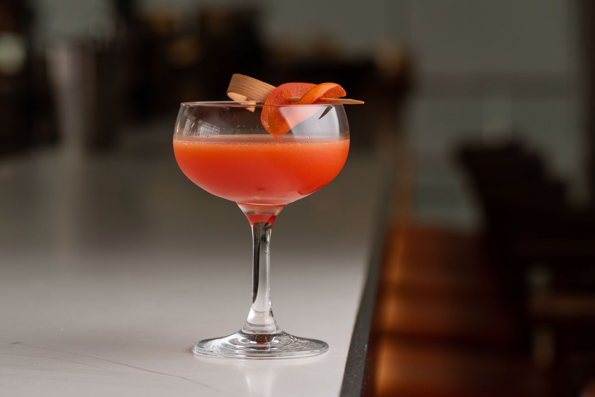 A light red coupe glass of a cocktail on the edge of a white table.