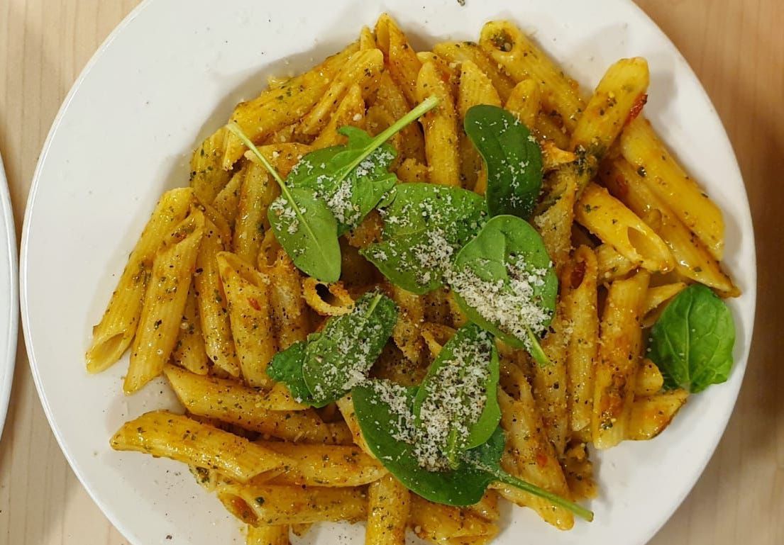 Penne with tomato and basil leaves on a white plate and wooden table