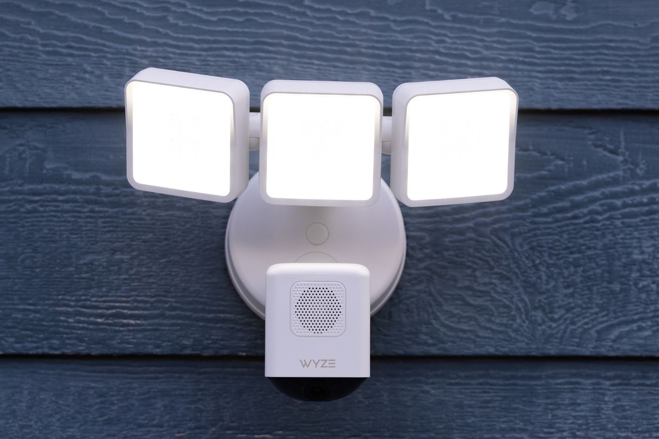 A photograph of the Wyze Cam Floodlight Pro in white mounted on a blue-gray wooden wall.