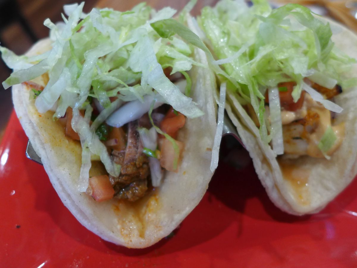Two double-corn-tortilla tacos heaped with shredded lettuce.
