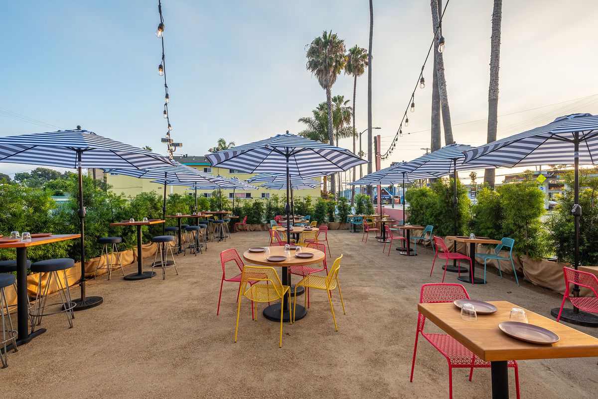 Front patio at Nueva in Venice with blue striped umbrellas and colorful metal chairs.
