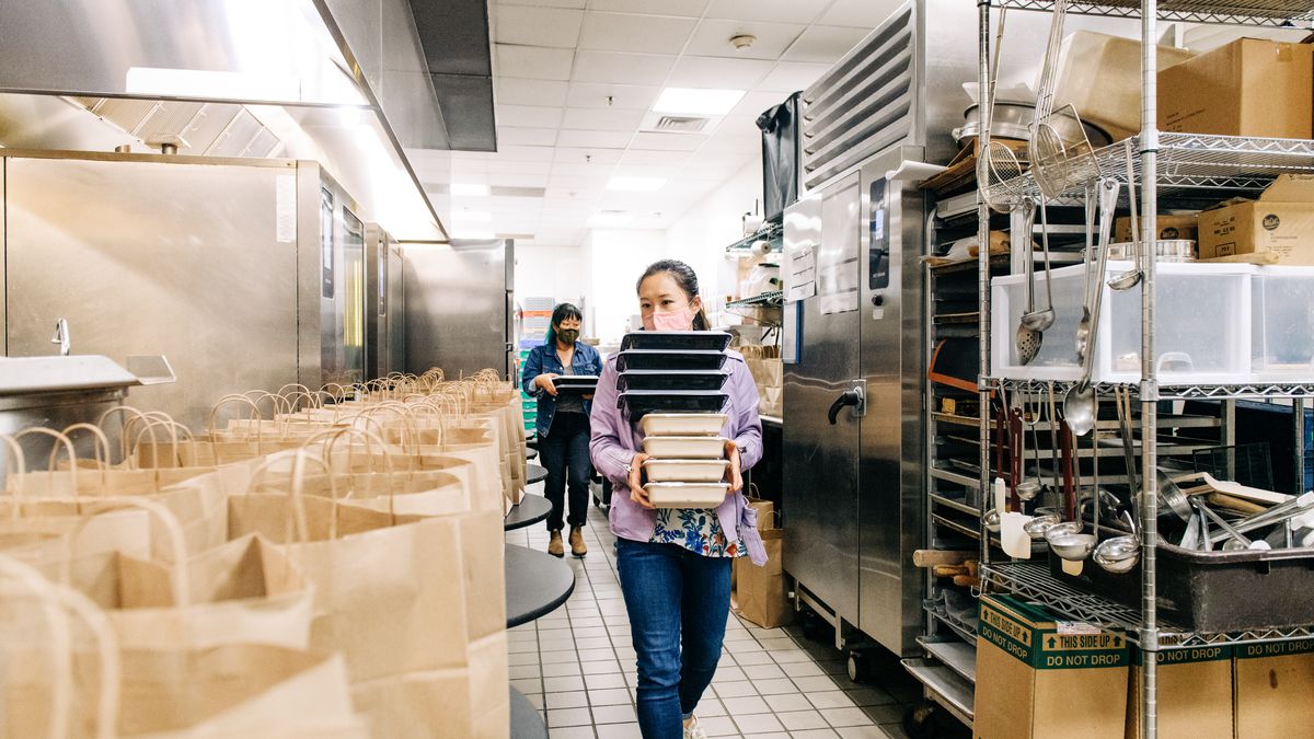 Chefs Stopping AAPI Hate volunteers Lillie Zheng and Helen Choe carry stacks of takeout boxes next to a table prepared with bags inside the kitchen at Moon Rabbit in D.C,