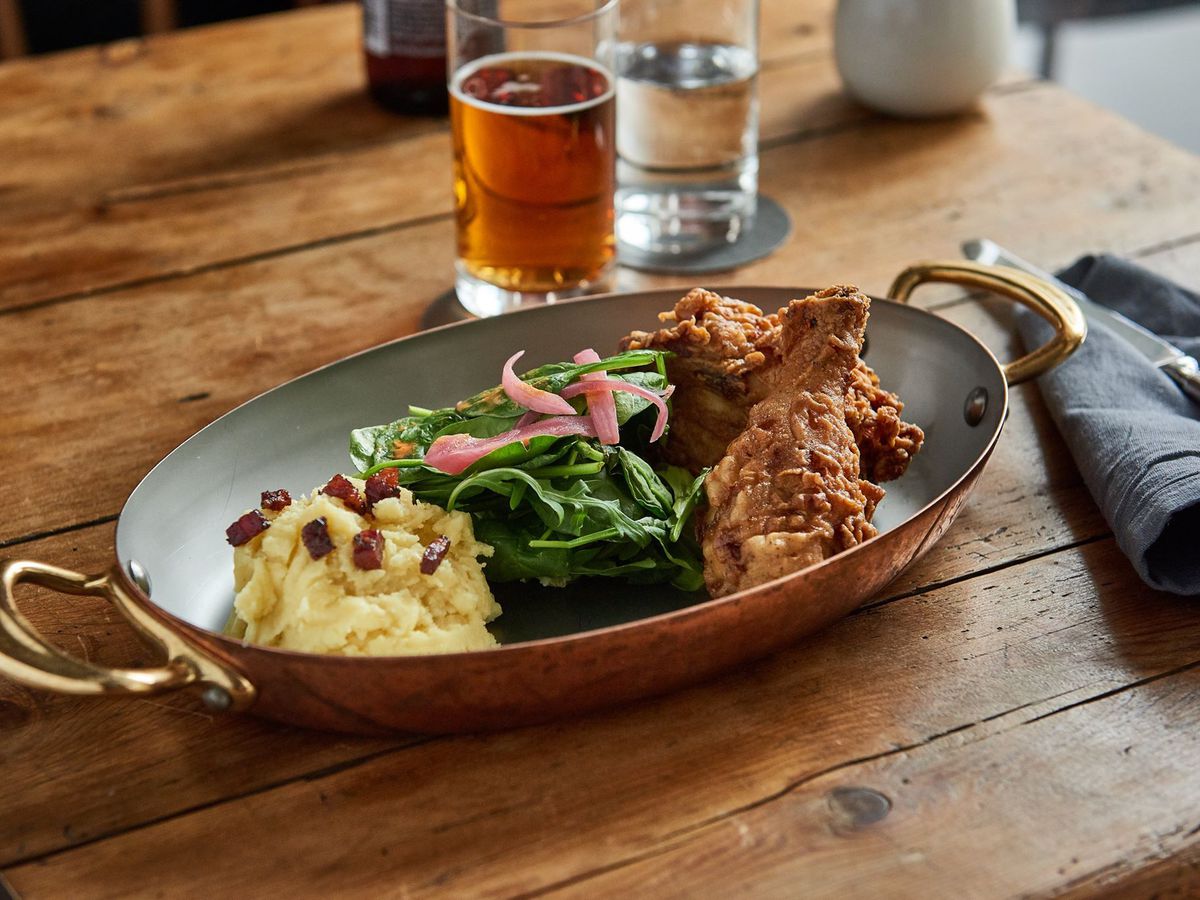 A metal serving shallow bowl with fried chicken, greens, and mashed potatoes.