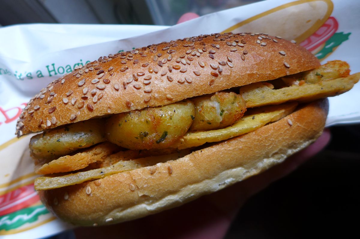 A sandwich on a sesame seed elongated roll with round small potatoes visible inside.