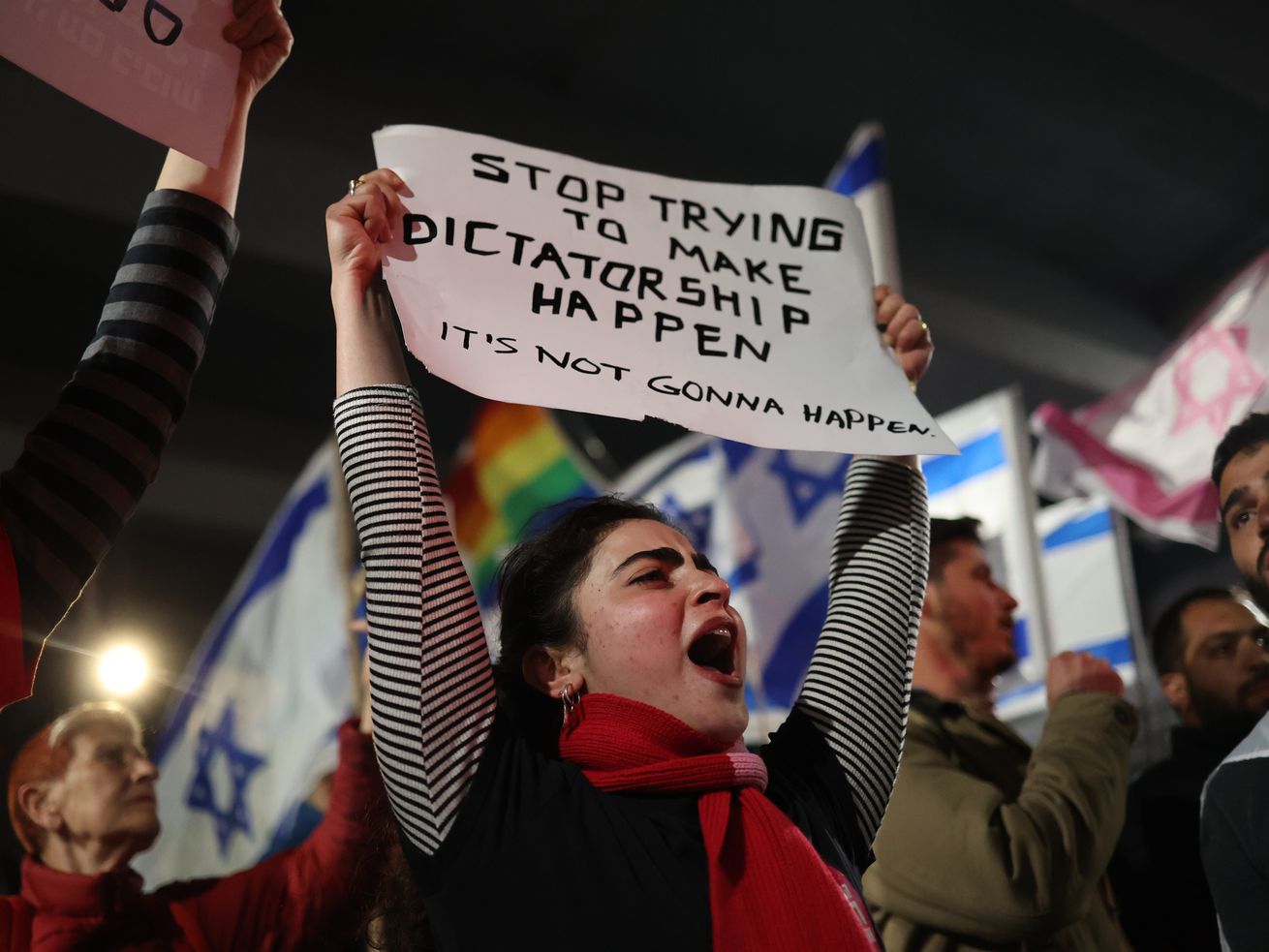A protester in a crowd holds a sign above her head that reads, “Stop trying to make dictatorship happen. It’s not gonna happen.”