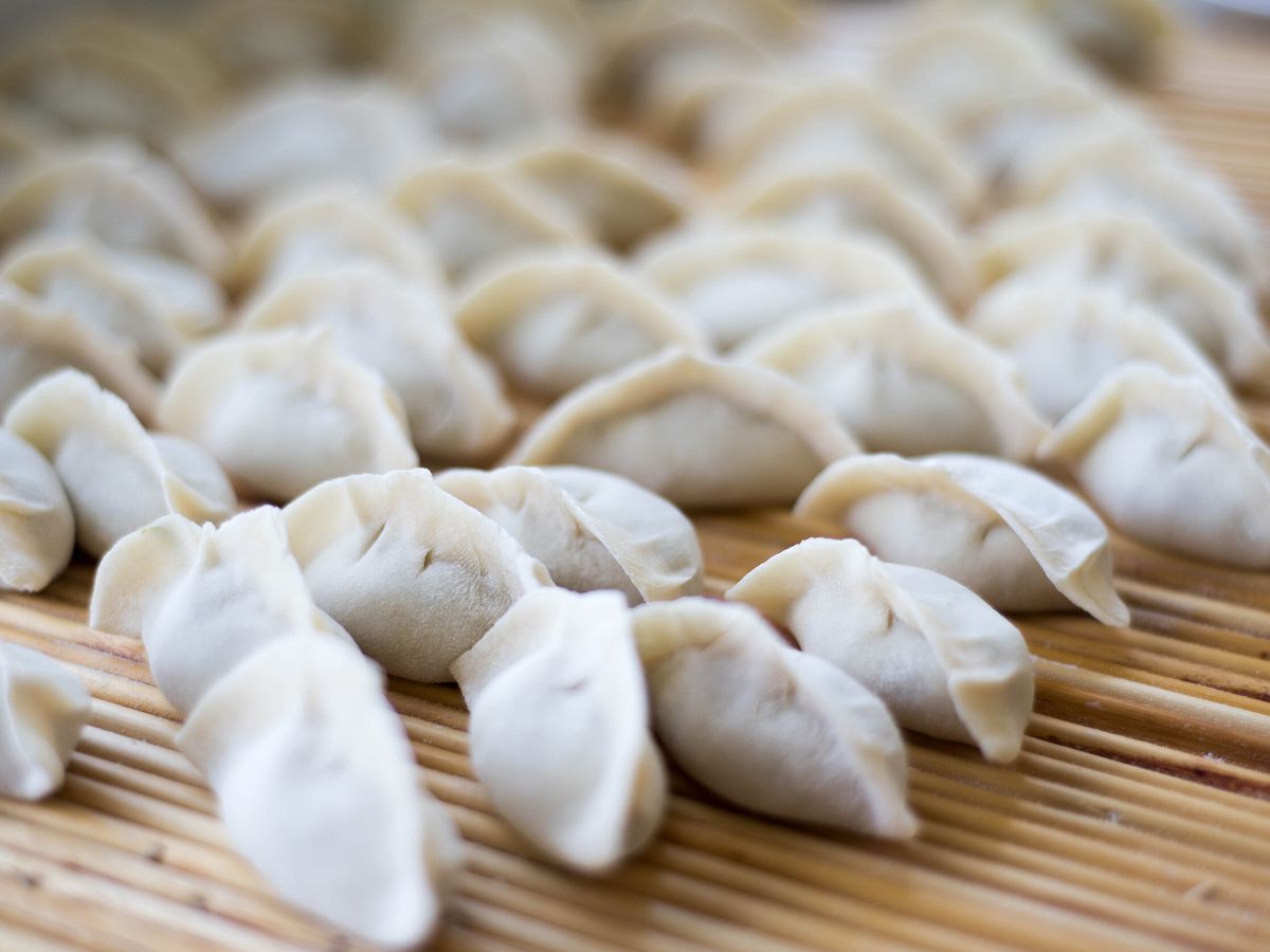 A collection of steamed dumplings on a slatted wooden tray, seen close up.