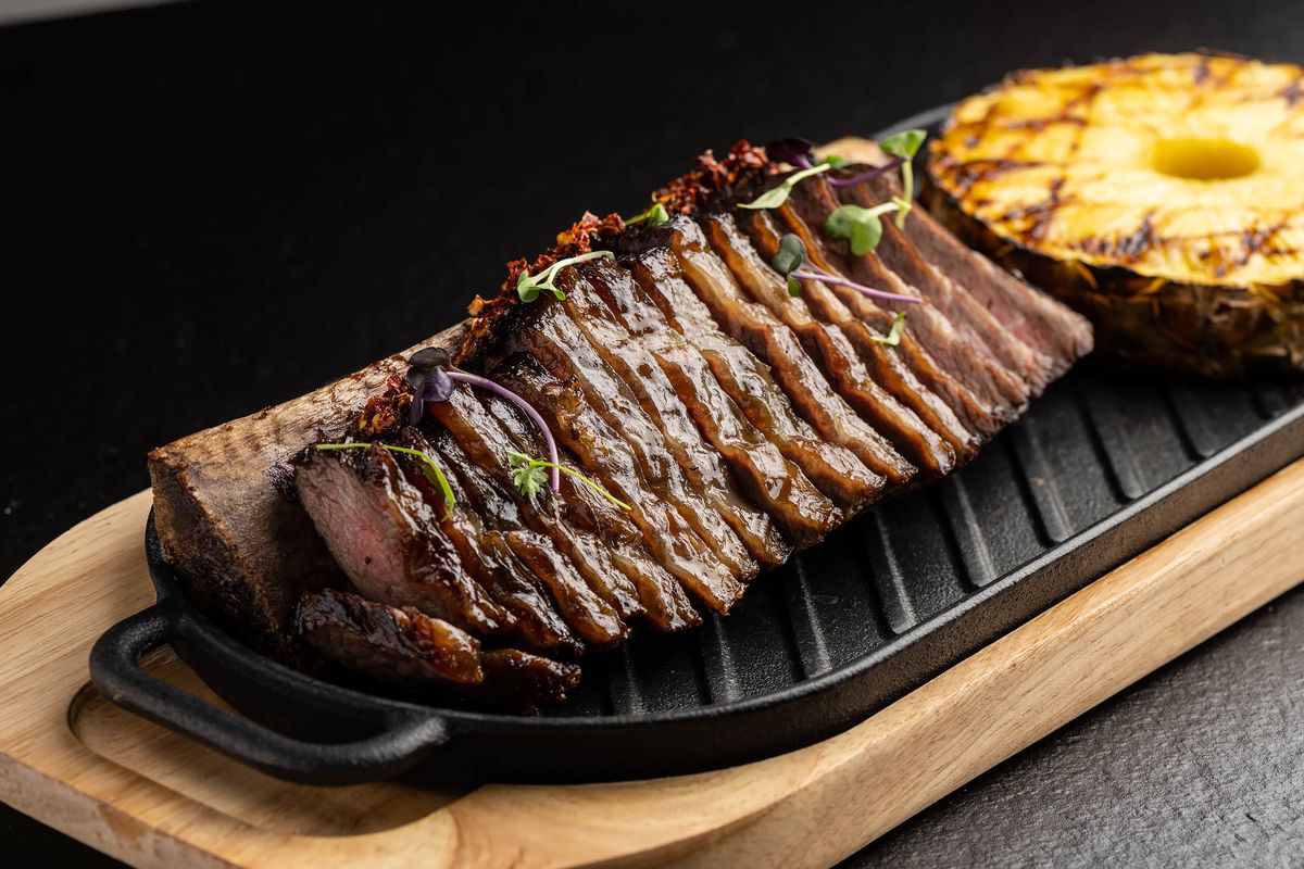 Slices of cooked, stewed beef on the bone next to grilled pineapple at a new restaurant.