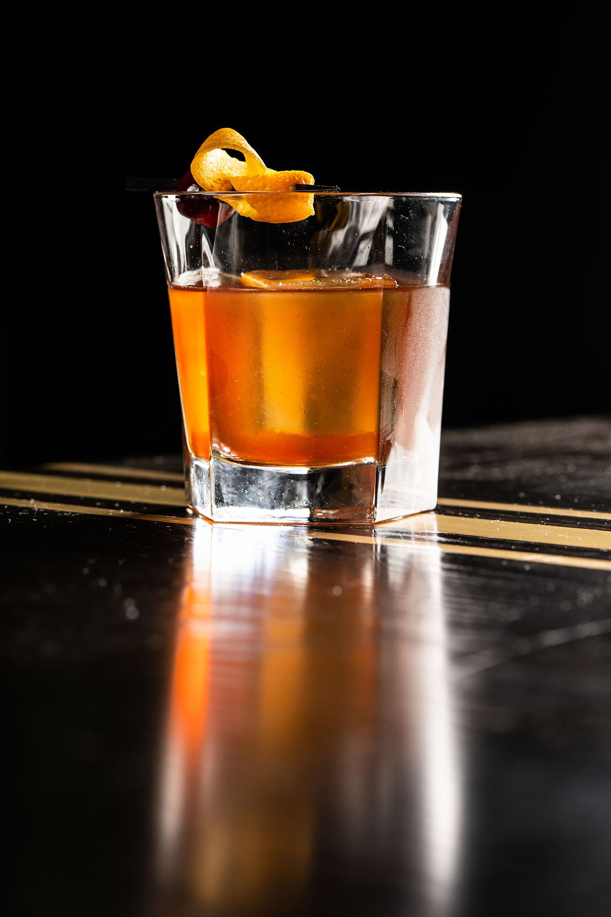 A simple cocktail with orange garnish on a black bartop.