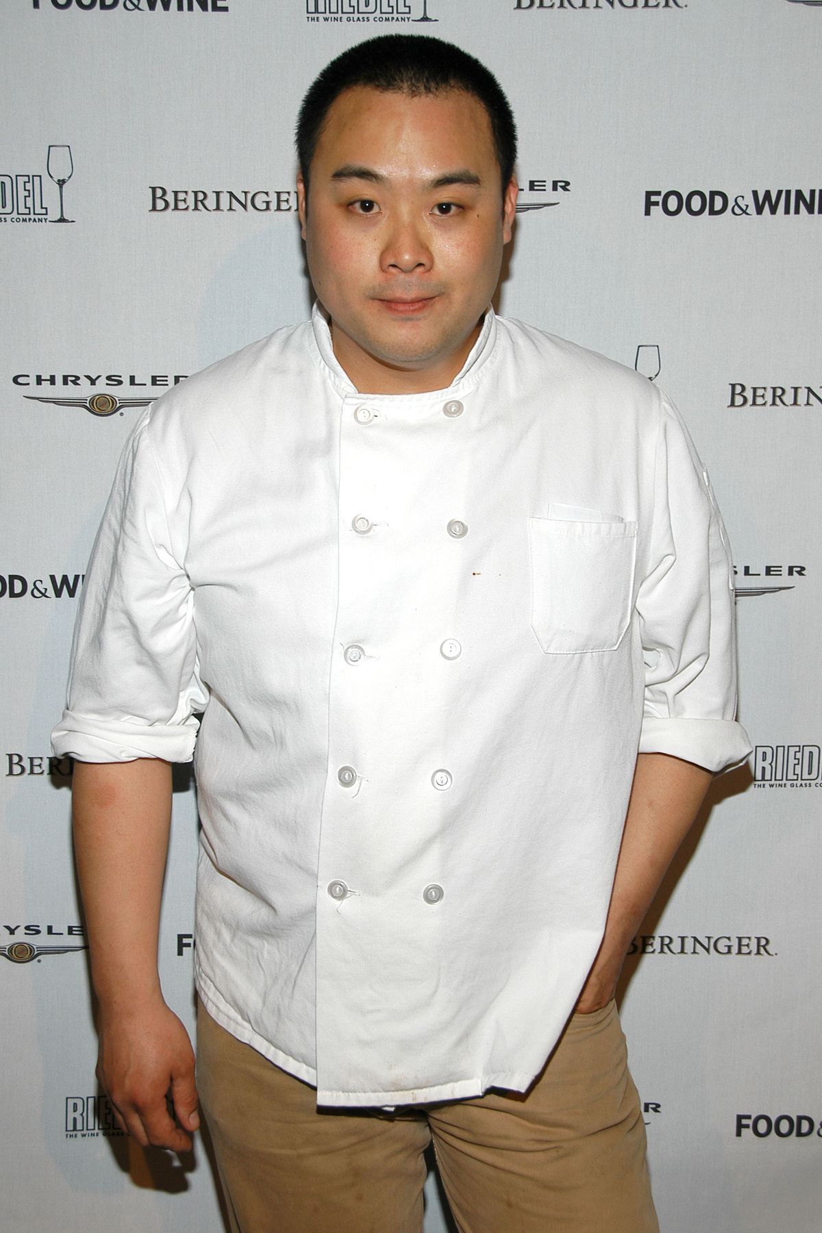 Chef David Chang, wearing a white chef’s shirt, stands in front of a backdrop at a Food and Wine event.