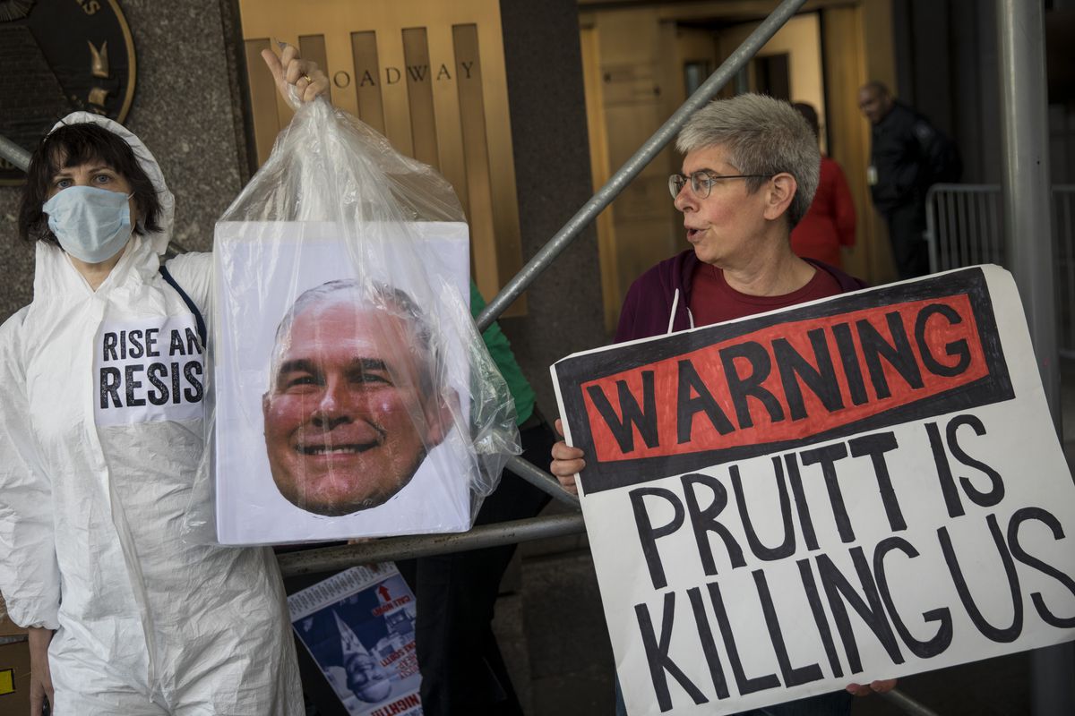 Protestors rallying against Environmental Protection Agency administrator Scott Pruitt: One is in a hazmat suit and carrying Pruitt’s picture sealed in a plastic bag, the other is holding a sign that reads, “Warning, Pruitt is killing us.”