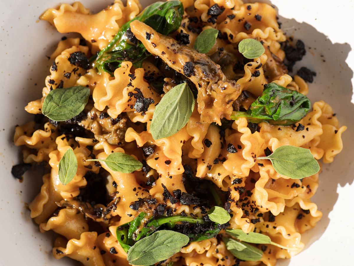From above, crinkle-edged pasta with basil leaves and dark crumbles.
