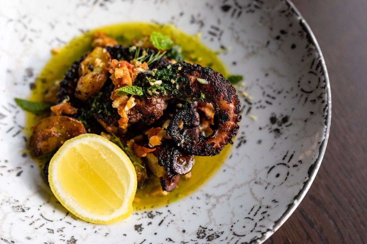 Wood fire-roasted octopus is topped with Sicilian tomato pesto, crispy potatoes, salsa verde, basil, parsley, and&nbsp;lemon 