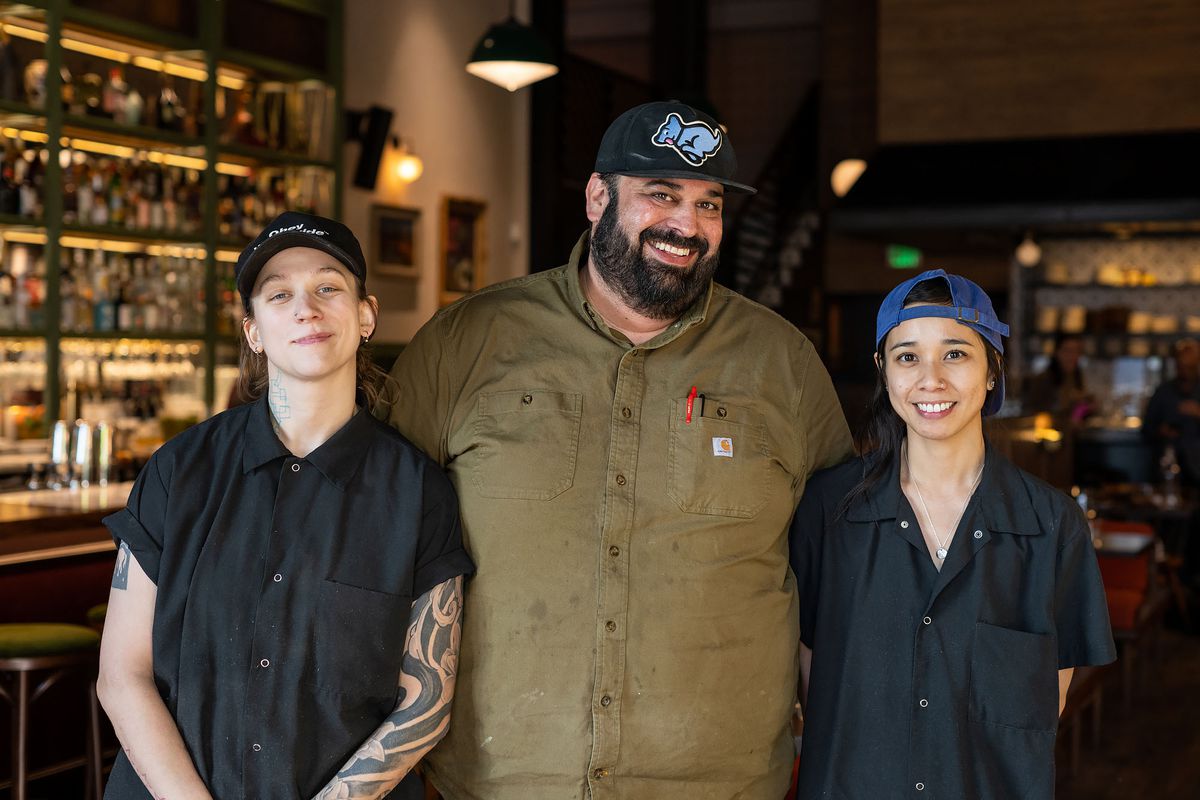 A trio of smiling faces stand arm over arm at the front of a new restaurant.