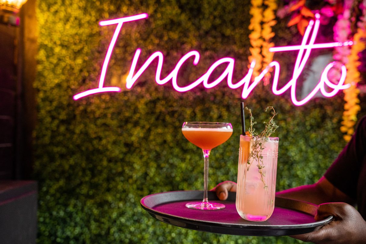 Two cocktails sit on a tray in front of a neon Incanto sign.