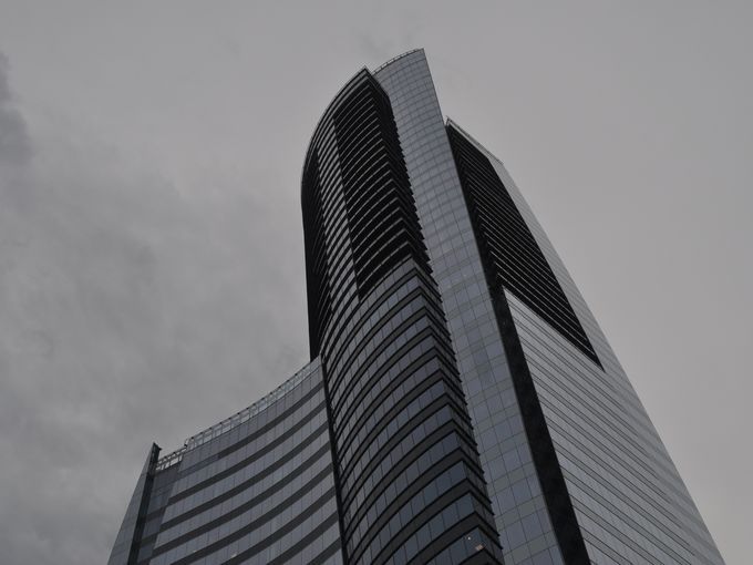 A towering, sweeping blue glass building against a grey sky.