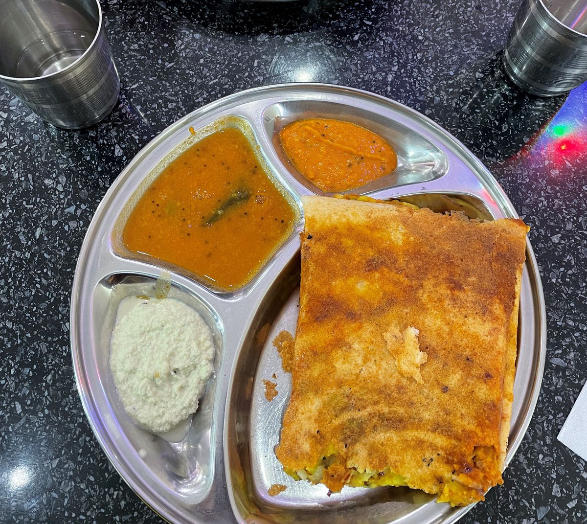A silver tray with a masala dosa, two orange chutneys, and one sploosh of yoghurt, each in their own compartments.