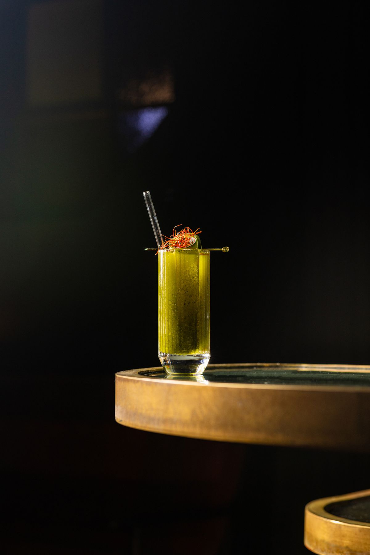 A green-tinted cocktail with straw on the edge of a table.