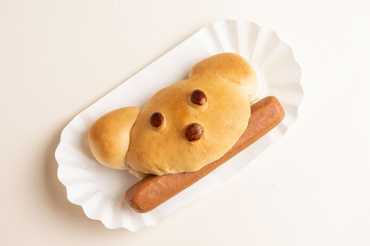 A puffy yellow bun with dogged burned eyes and a boiled hot dog on a paper sleeve.