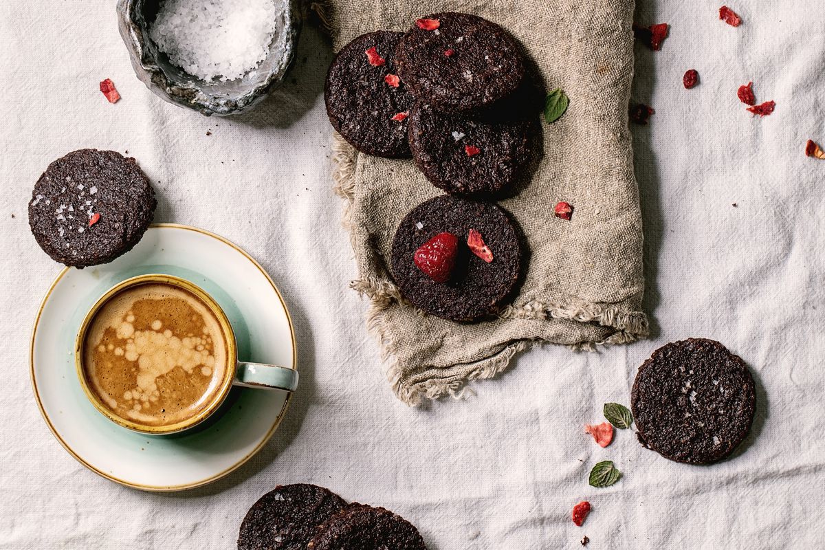 Homemade dark chocolate salted brownies cookies decorated by dried and fresh raspberries, with salt flakes, berries, mint, milk and cup of coffee over white cotton cloth. Flat lay, space