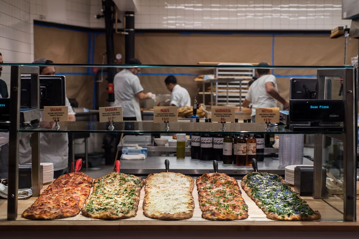 An array of long, thin pizzas available to be cut into squares Roman style at a glowing restaurant named Triple Beam.