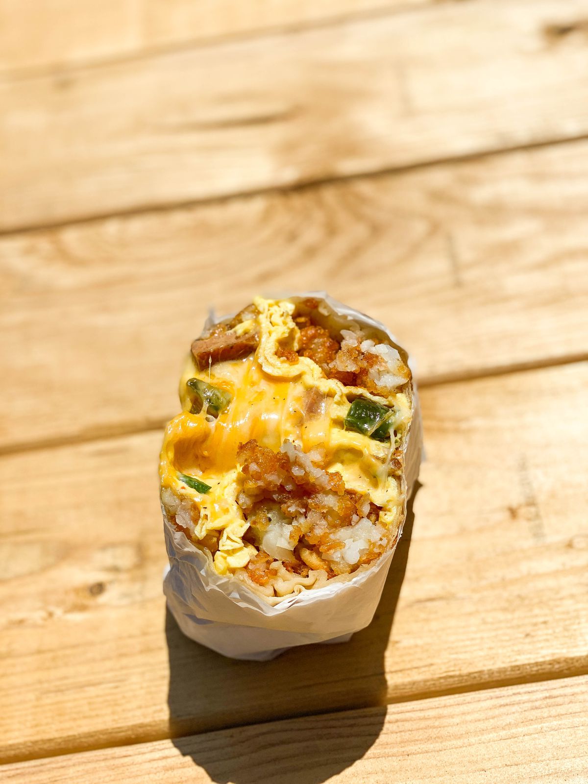 A split vertical look at a cheesy breakfast burrito on a bright wooden table.