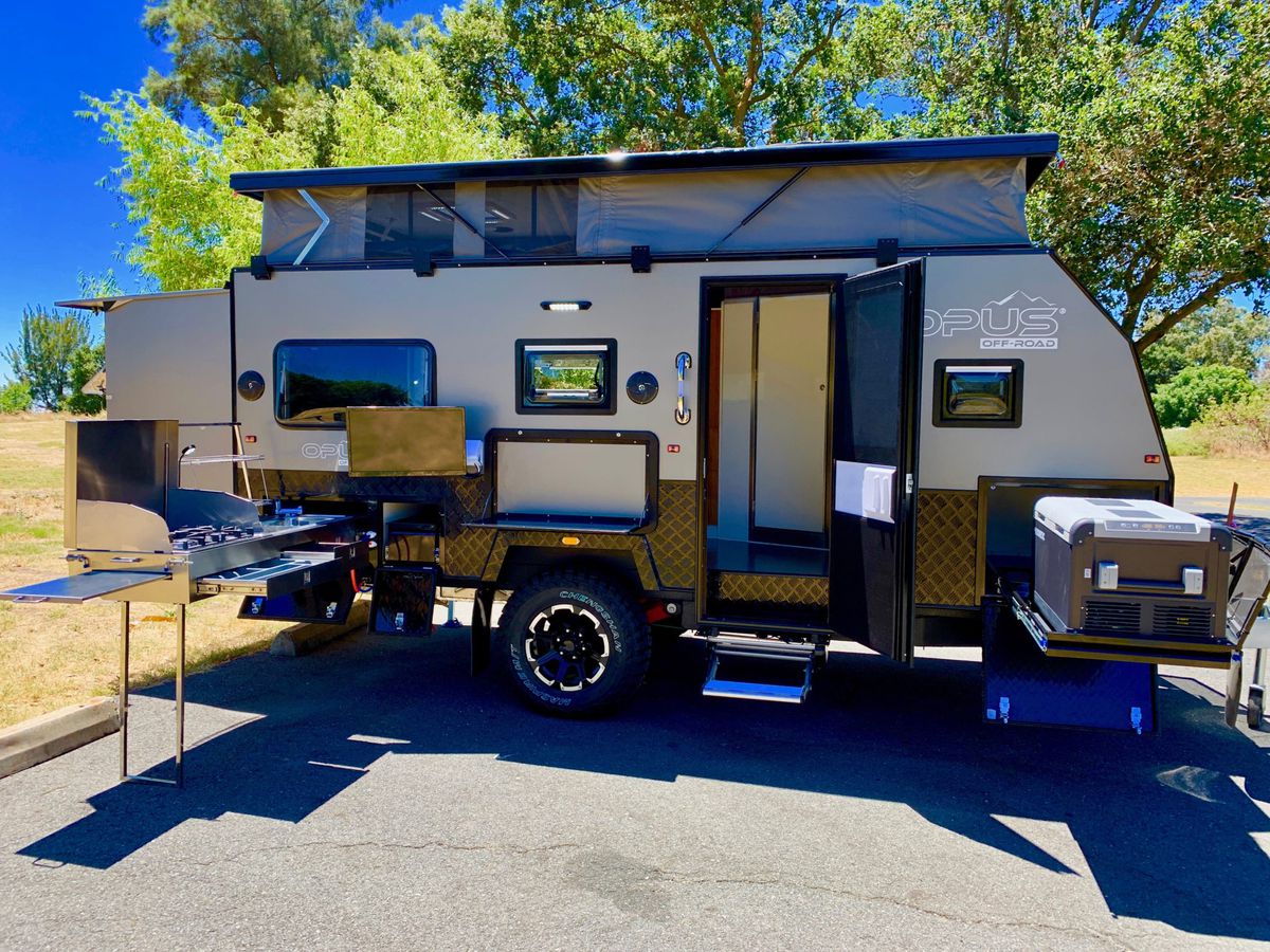 A side view of the trailer, with a closer look at the stainless steel stovetop, prep station, pull-out fridge, and an open door looking inside. 