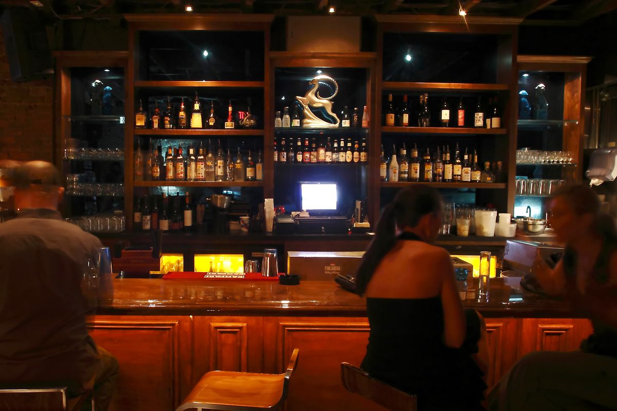 A dark bar with a woman sitting at the bar.